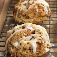 Three glazed cinnamon bun scones on a wire rack.