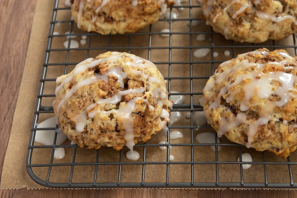 Four cinnamon bun scones on a wire rack. Glaze is running off them.