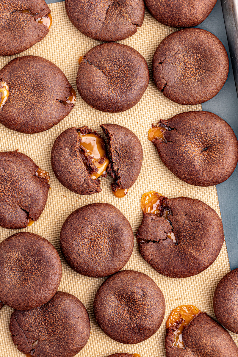 Overhead view of chocolate caramel cookies on silpat with some broken to show gooey middles