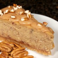 A slice of Praline Cheesecake on a plate next to some pecans