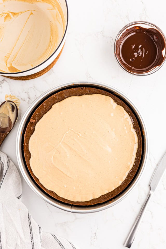 Peanut butter and white chocolate topping spread over chocolate peanut butter cheesecake
