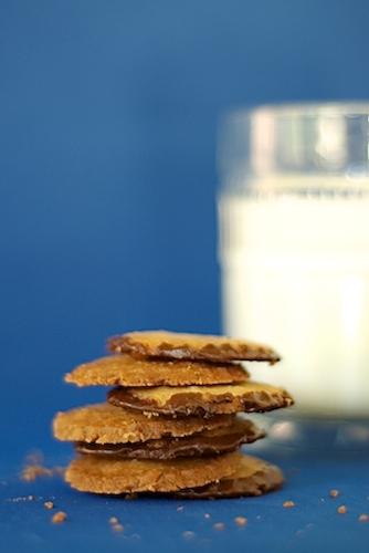 A stack of pecan shortbread cookies rimmed with chocolate, with a glass of milk in the background.