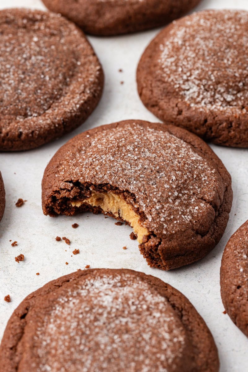 Chewy peanut butter-filled chocolate cookies on countertop with one bitten into to show filling