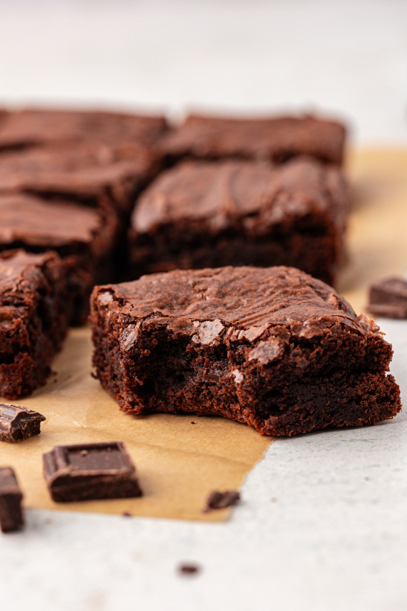 Rich double chocolate brownies on parchment paper, with one bitten in corner