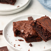 Two double chocolate brownies on plate, with one bitten in corner