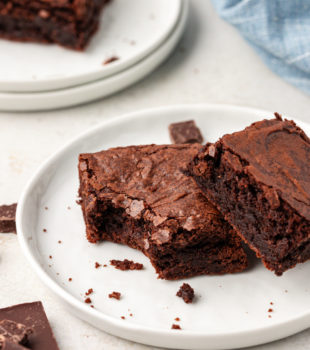 Two double chocolate brownies on plate, with one bitten in corner