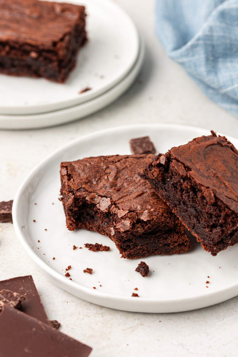 Two double chocolate brownies on plate, with one bitten in corner