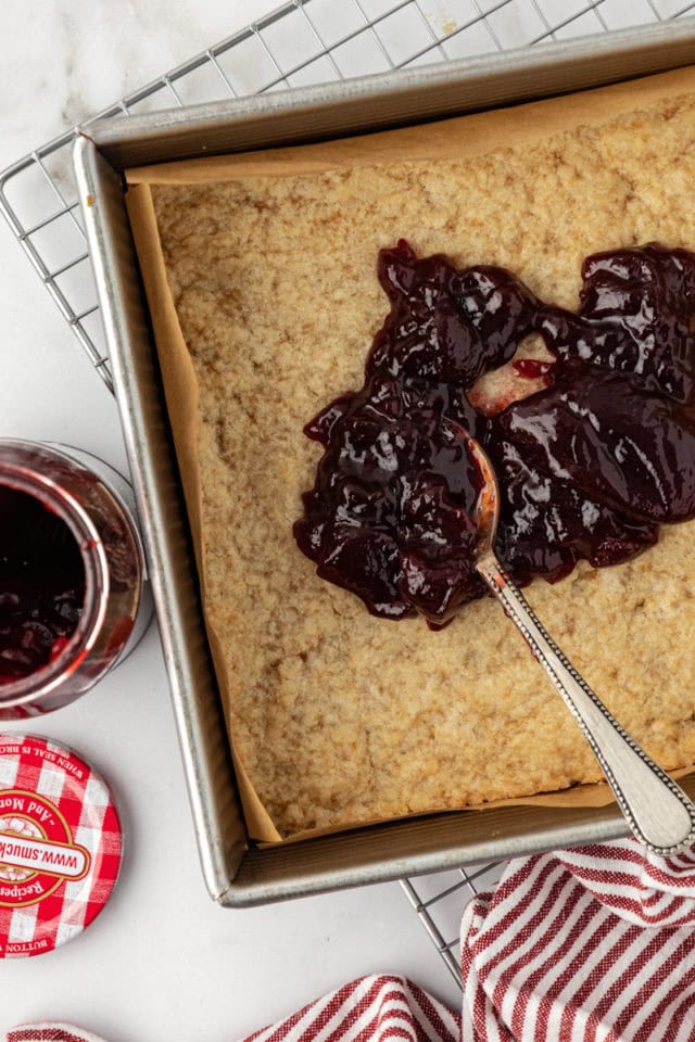 Overhead view of raspberry preserves being spread onto crust with spoon