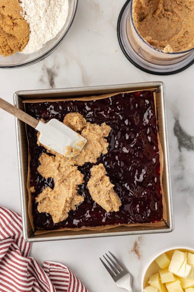 Overhead view of hazelnut layer being spread over preserves for raspberry crumble bars