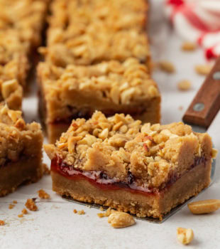 Homemade peanut butter and jelly bars on countertop with one bar on spatula