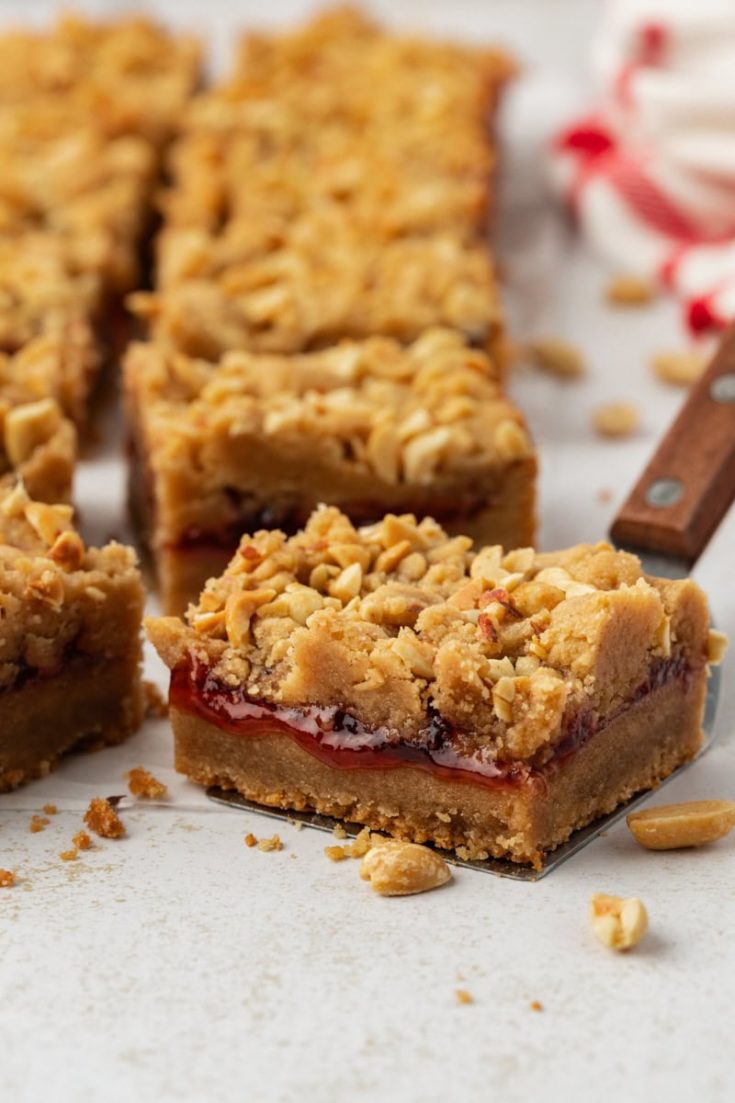Homemade peanut butter and jelly bars on countertop with one bar on spatula