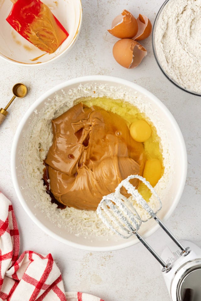 Overhead view of eggs, vanilla, and peanut butter added to mixing bowl