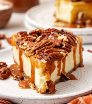 Slice of salted caramel cheesecake on plate with pecans on top