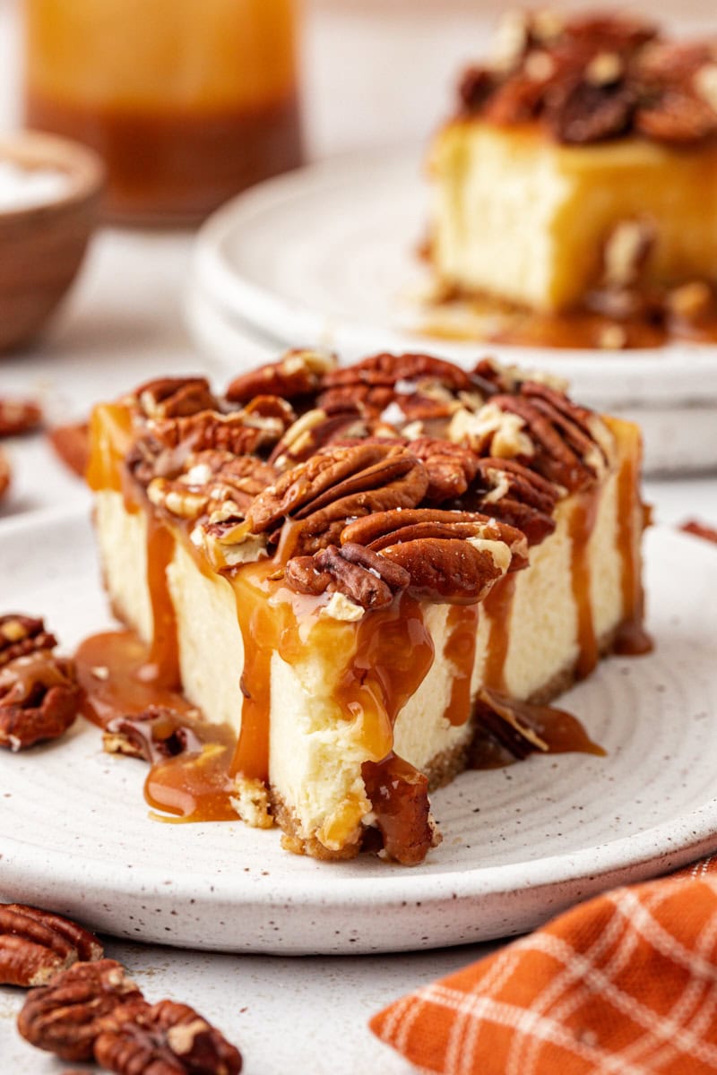 Slice of salted caramel cheesecake on plate with pecans on top