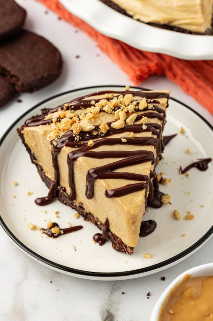 Slice of peanut butter pie on plate with fudge sauce and peanuts