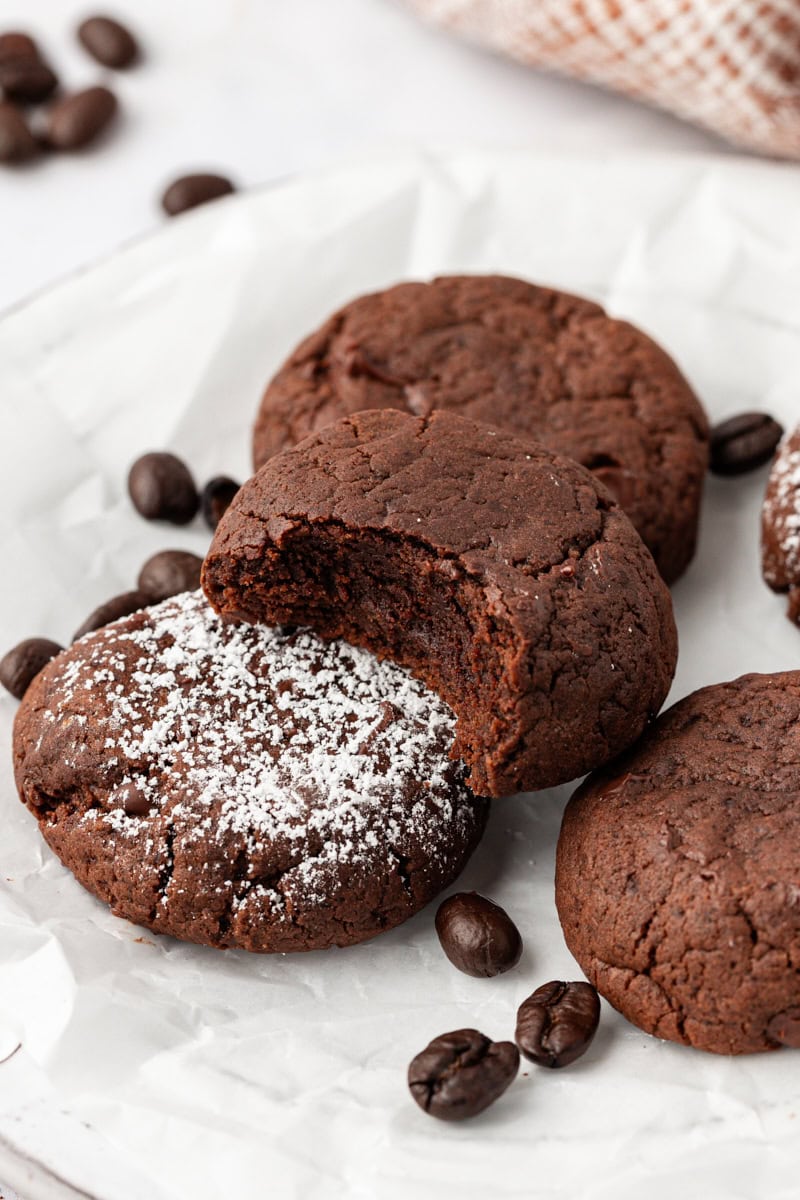 A few chocolate espresso cookies on parchment paper, with one cookie bitten to show fudgy texture