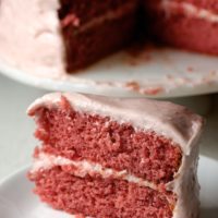 Slice of strawberry cake on plate with remaining cake in background