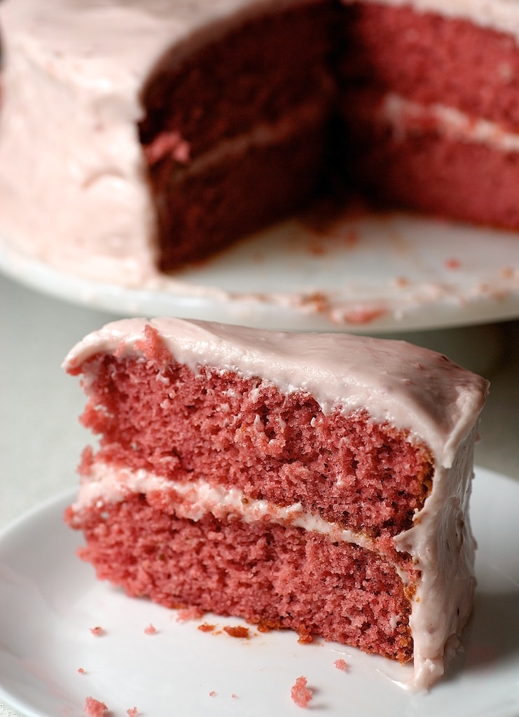 Slice of strawberry cake on plate with remaining cake in background