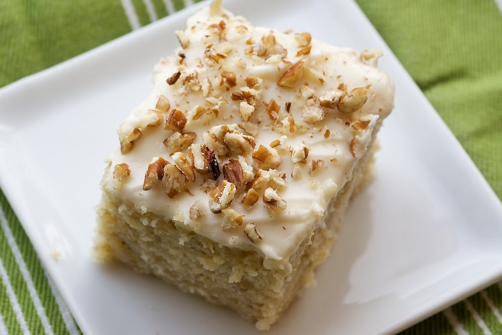 A square of banana cake on a white square plate on a green and white striped table cloth