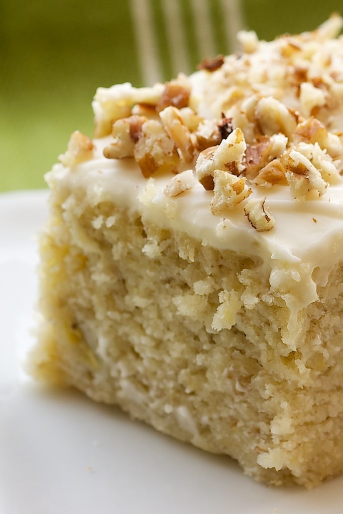 Closeup shot of square of banana cake topped with cream cheese frosting and chopped walnuts