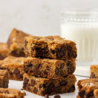 Stack of 3 fleur de sel chocolate chip blondies with additional blondies and glass of milk in background