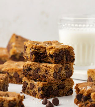 Stack of 3 fleur de sel chocolate chip blondies with additional blondies and glass of milk in background