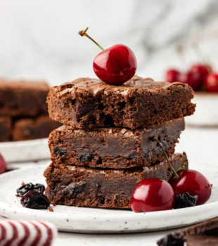 Three dark chocolate cherry brownies stacked on plate