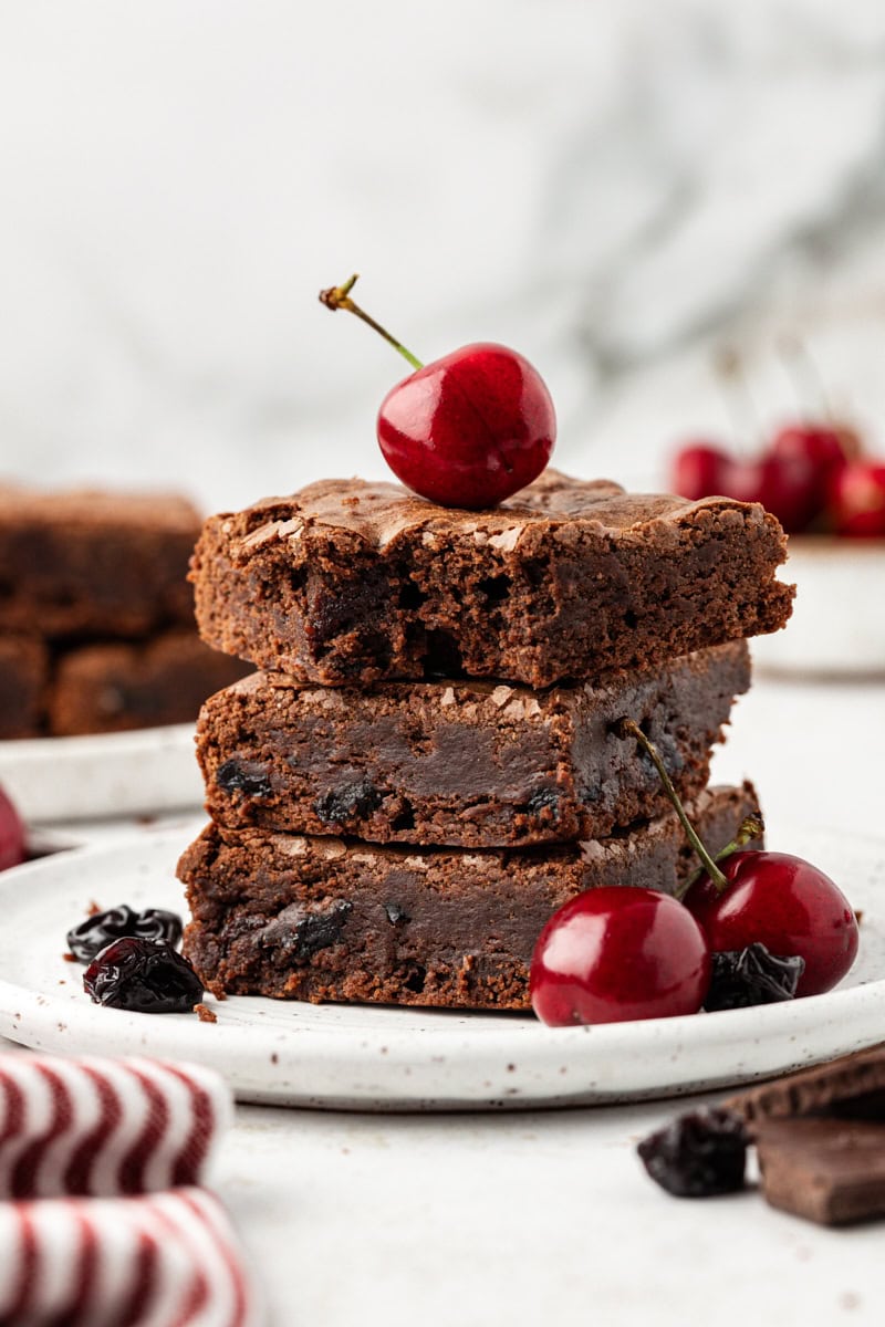 Three dark chocolate cherry brownies stacked on plate