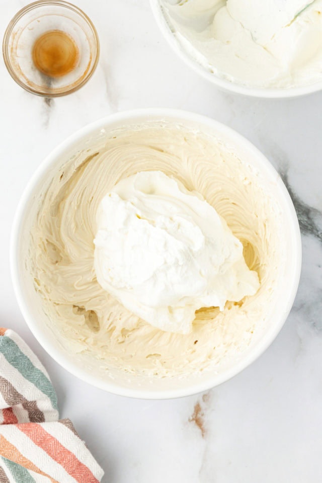 Overhead view of whipped cream added to cream cheese mixture in bowl