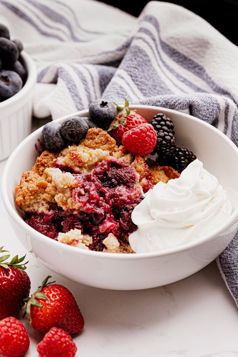 Bowl of mixed berry cobbler with whipped cream and fresh berries