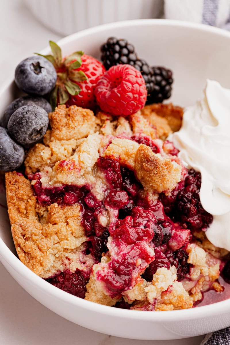 Mixed berry cobbler in bowl with fresh berries and whipped cream