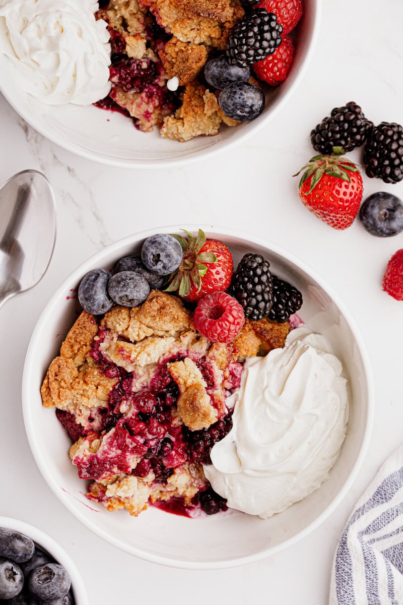 Two bowls of mixed berry cobbler with whipped cream and fresh berries