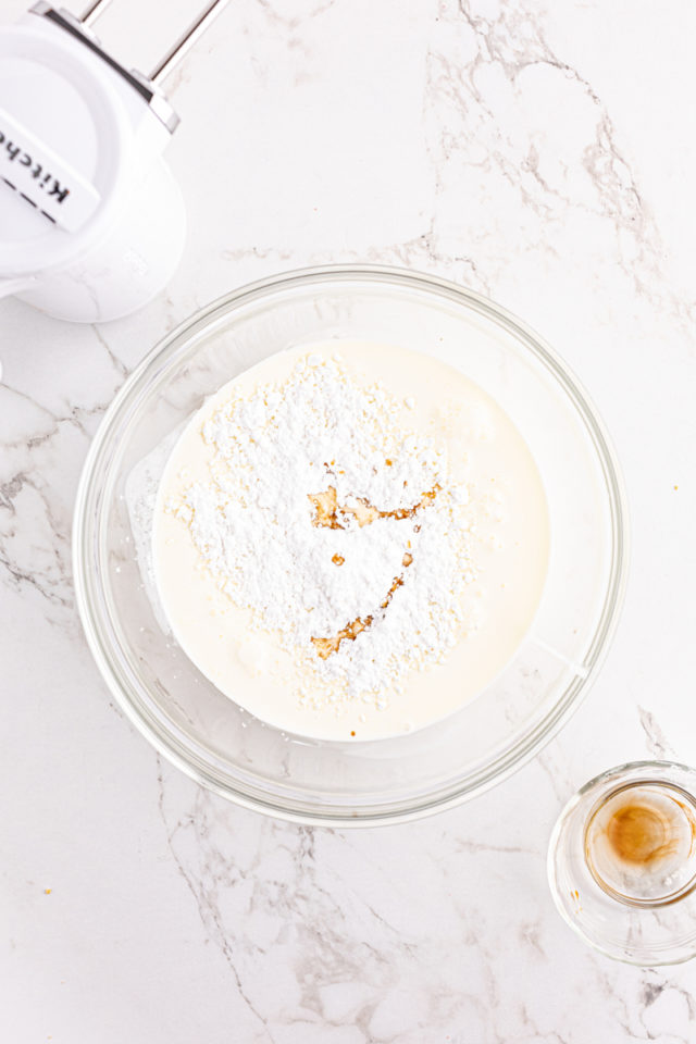 Overhead view of vanilla, powdered sugar, and heavy cream in mixing bowl