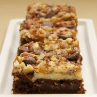 3 cream cheese brownies with toffee and pecans lined up on rectangular tray