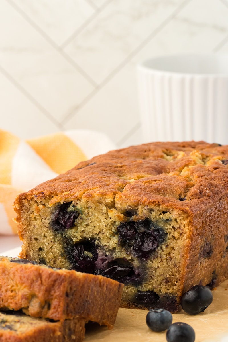 Banana blueberry bread on a cutting board with fresh blueberries.