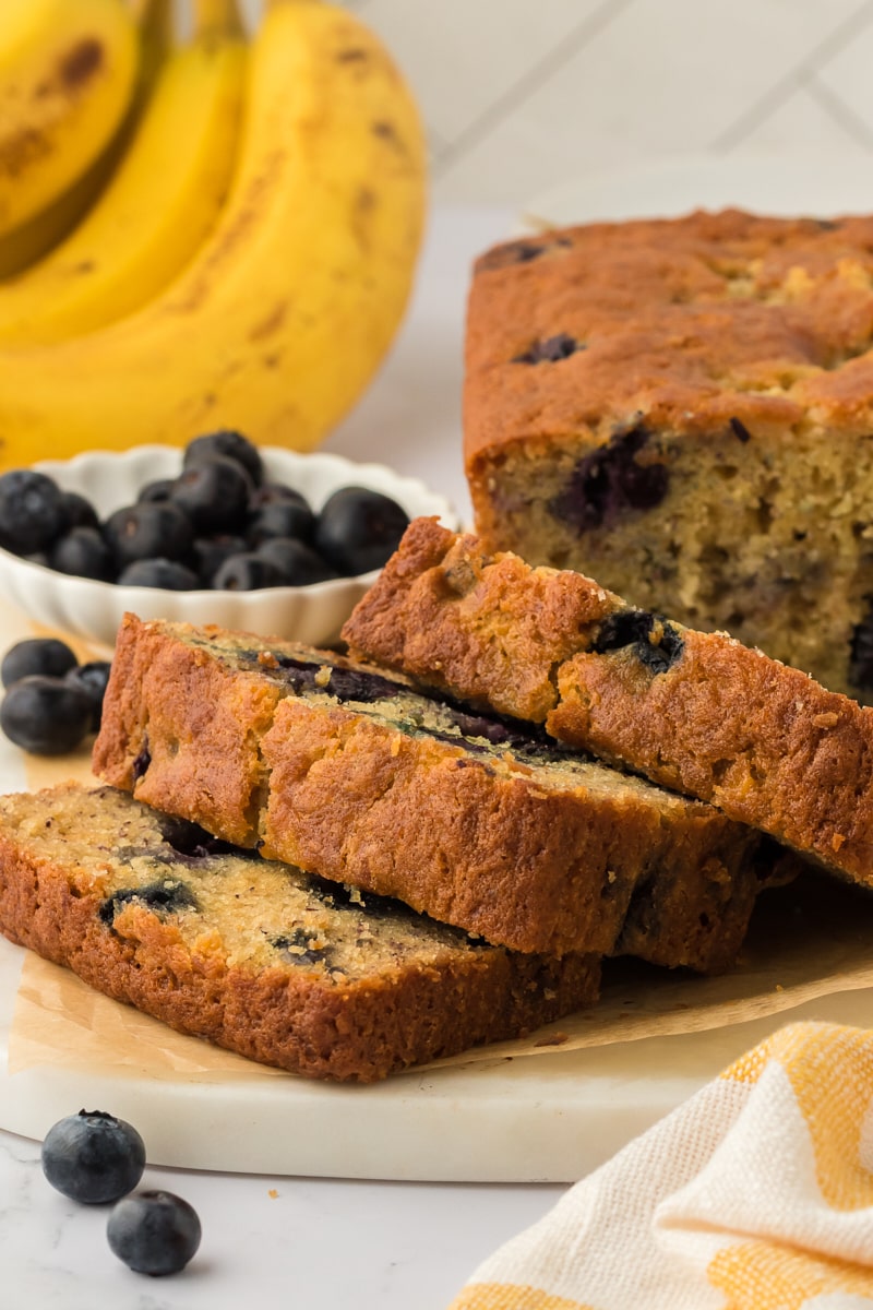 Slices of blueberry banana bread stacked on a cutting board.