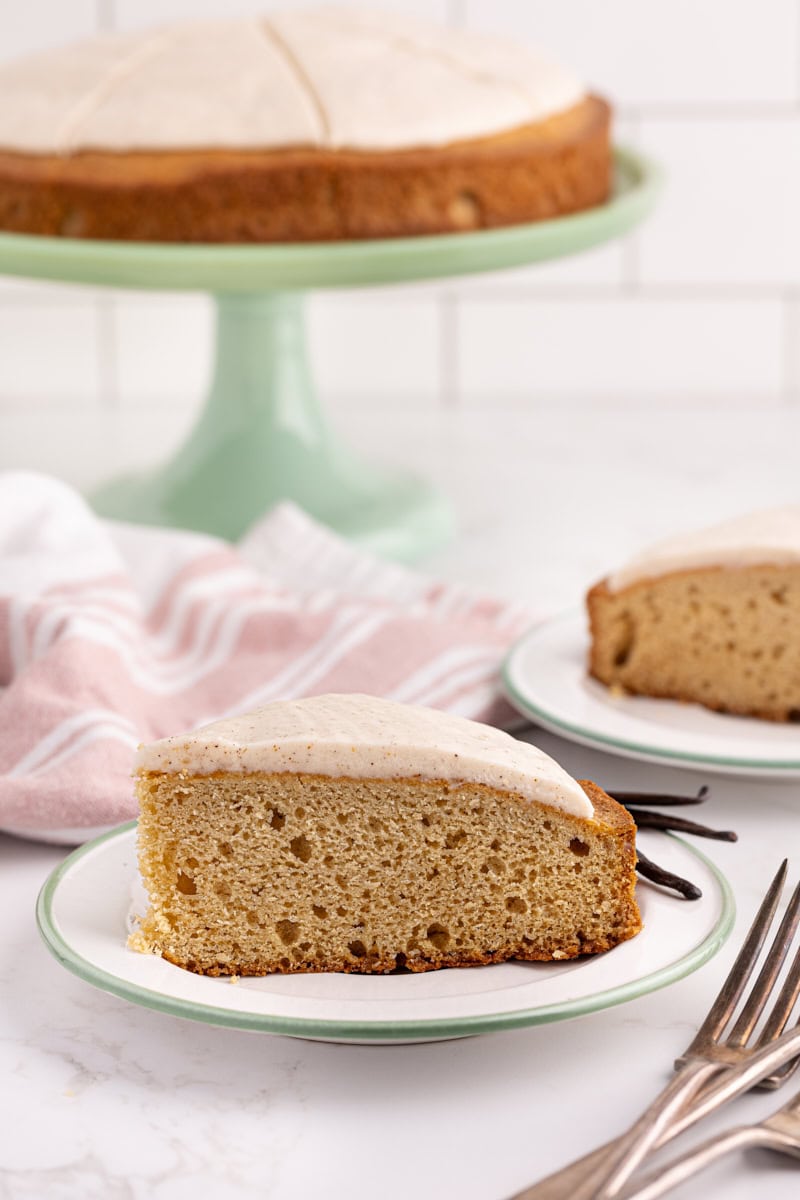 Two plates of vanilla bean cake, with remaining cake on cake stand in background