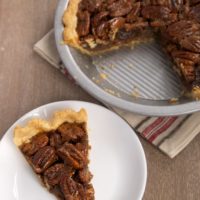 slice of Brown Butter Pecan Pie on a white plate with remaining pie in a pie plate