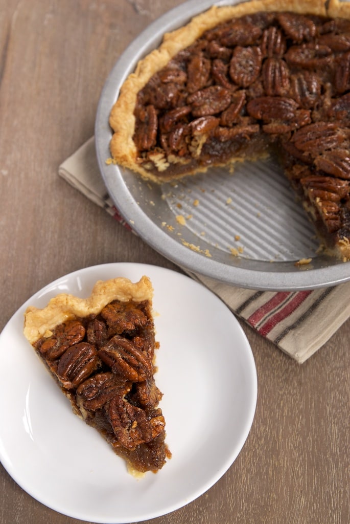slice of Brown Butter Pecan Pie on a white plate with remaining pie in a pie plate