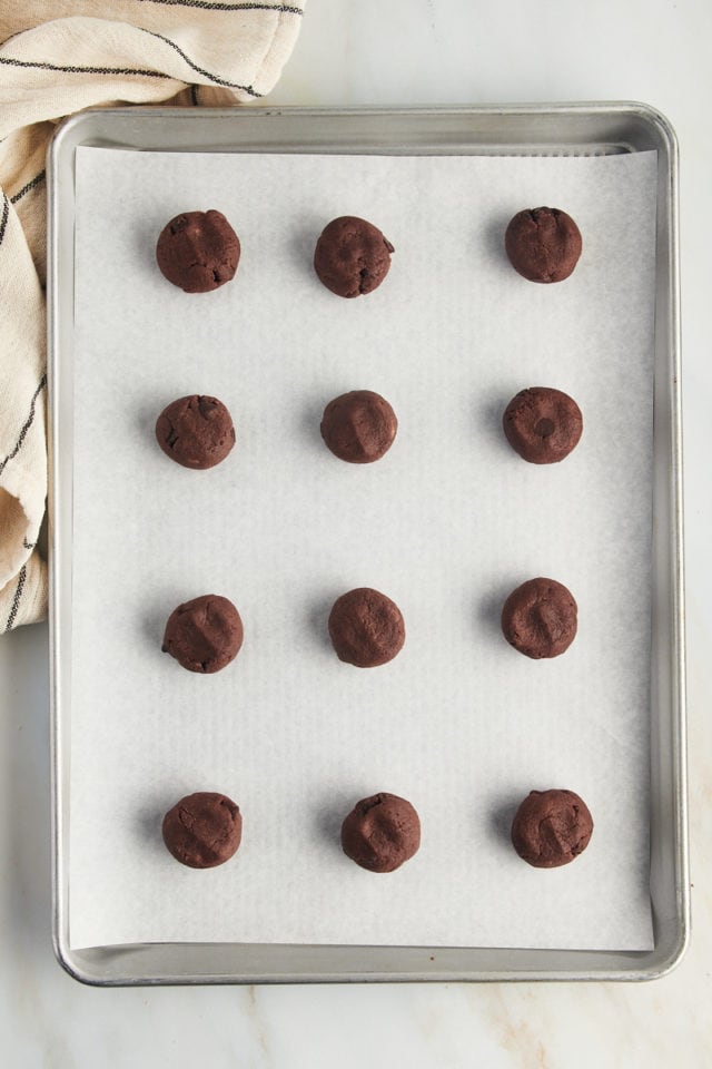 Overhead view of chocolate chocolate chip cookie dough balls on parchment-lined pan