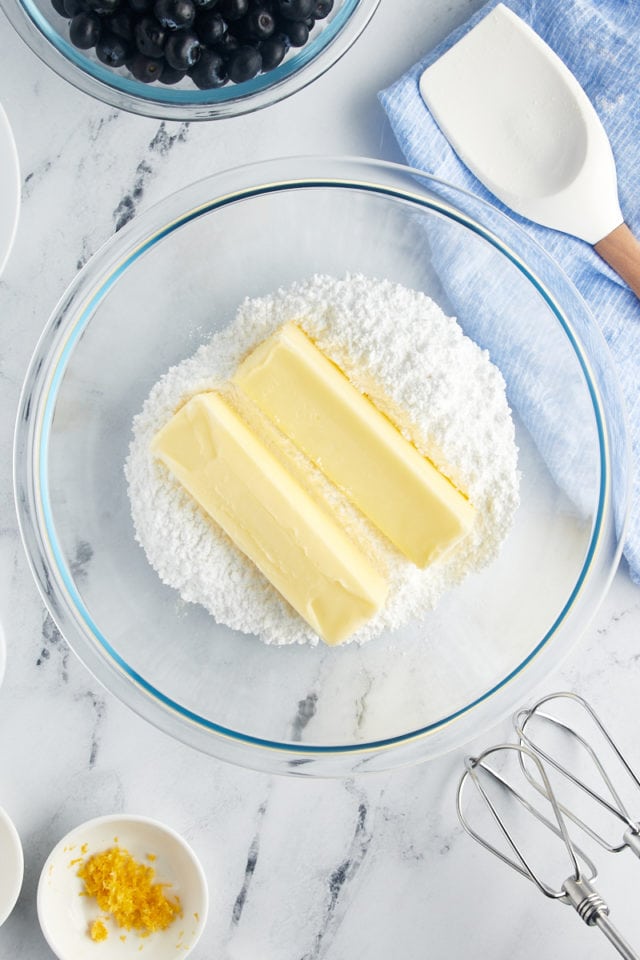 Two sticks of butter in a bowl of powdered sugar.