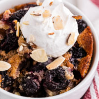 Brown butter cherry cobbler in bowl topped with dollop of whipped cream and almonds