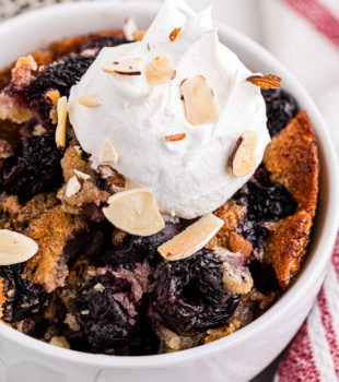Brown butter cherry cobbler in bowl topped with dollop of whipped cream and almonds