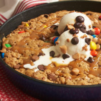 Cast iron skillet cookie topped with ice cream, chocolate chips M&Ms, and caramel