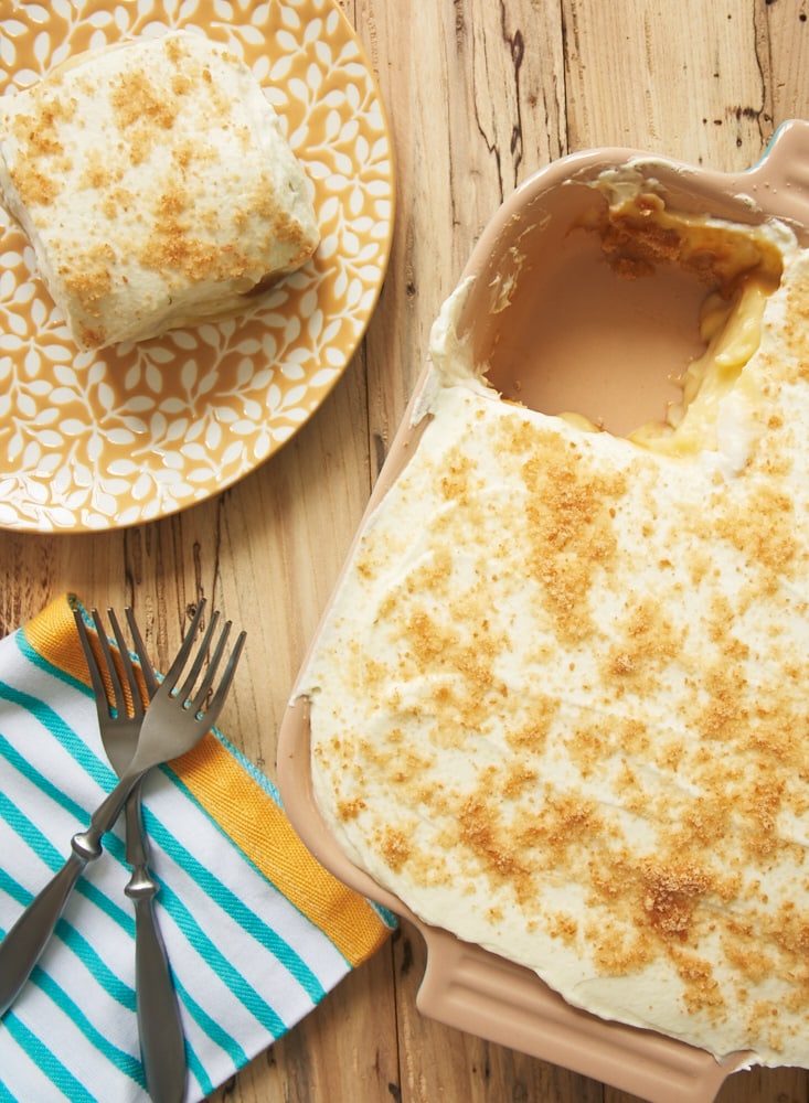 A pan of banana pudding bars with one missing, which is placed on a plate next to the pan.