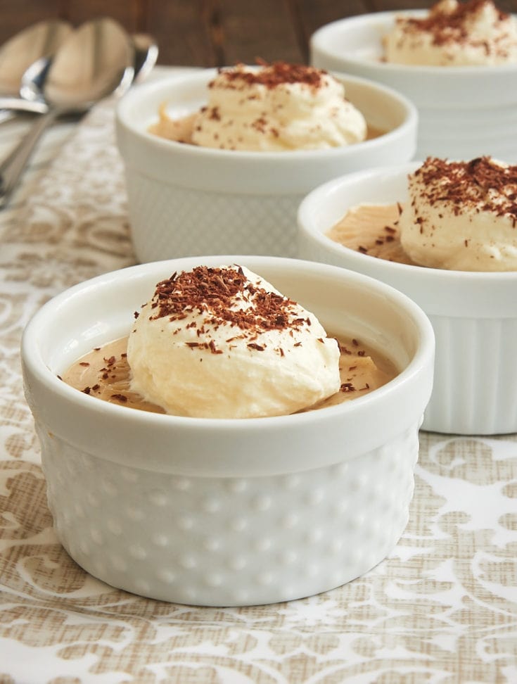 Peanut Butter Pudding served in white ramekins and topped with sweetened whipped cream and cocoa powder