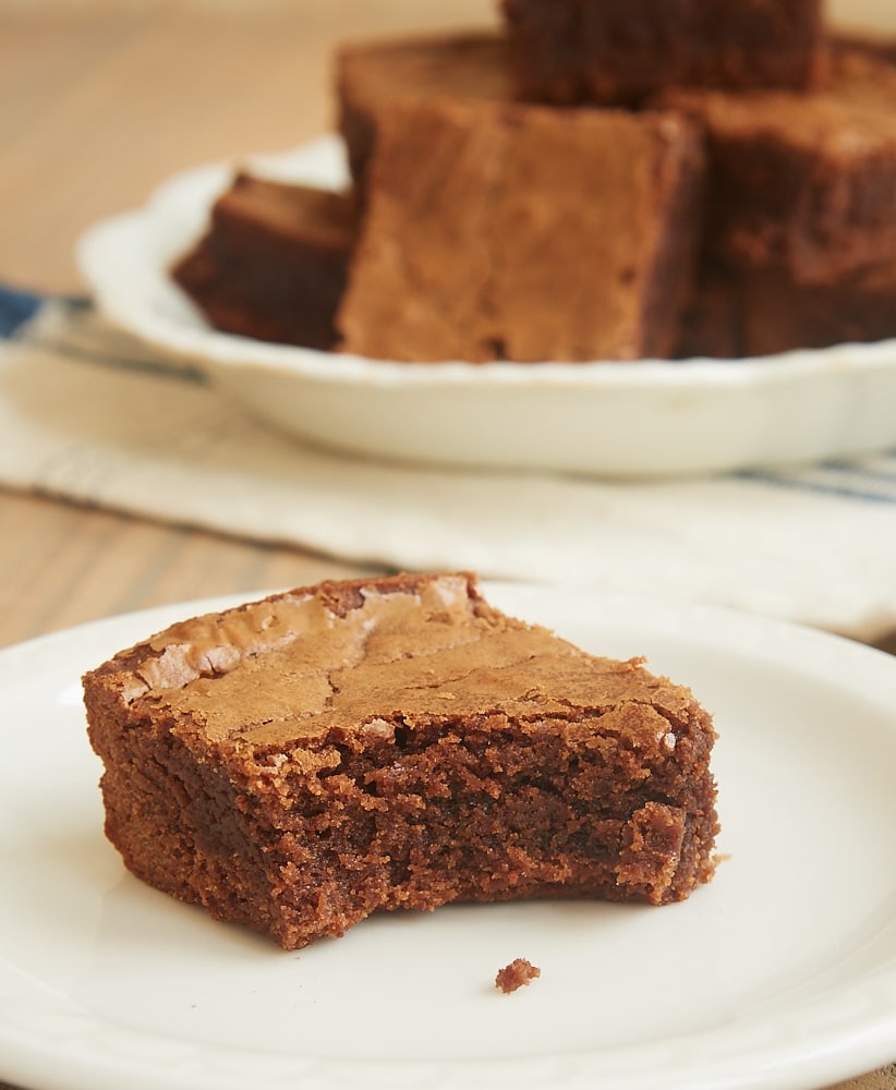 A brownie on a plate with a bite taken out of the corner.