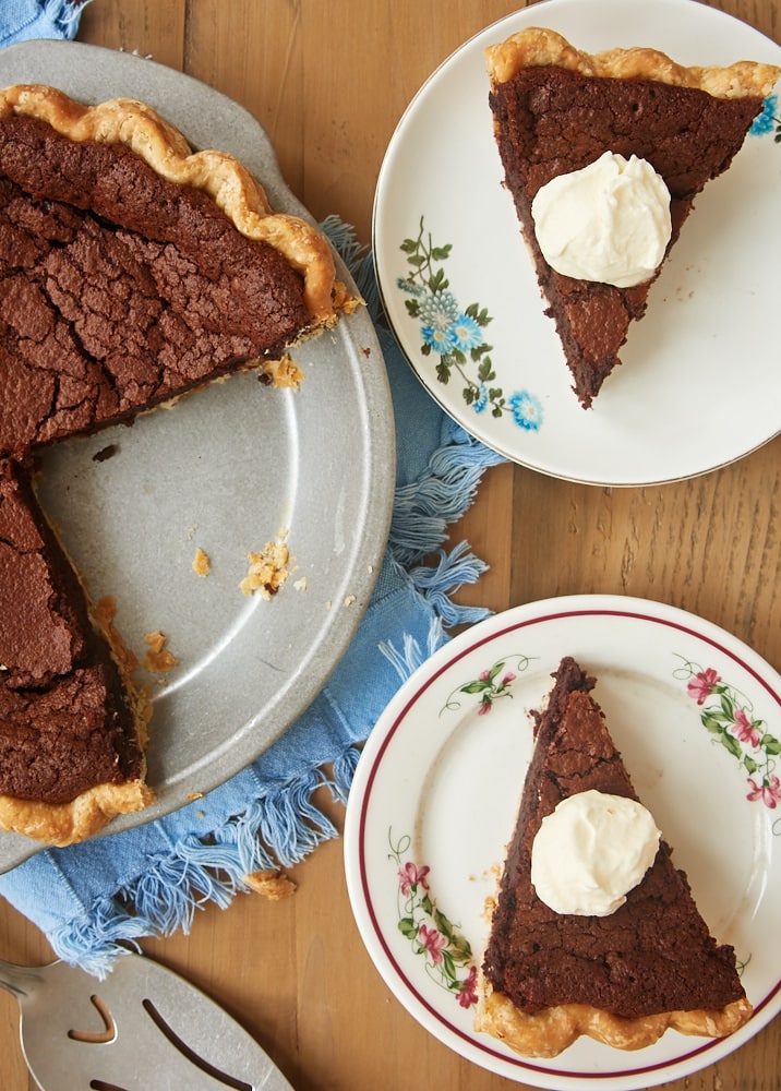Two slices of chocolate chess pie on plates topped with whipped cream
