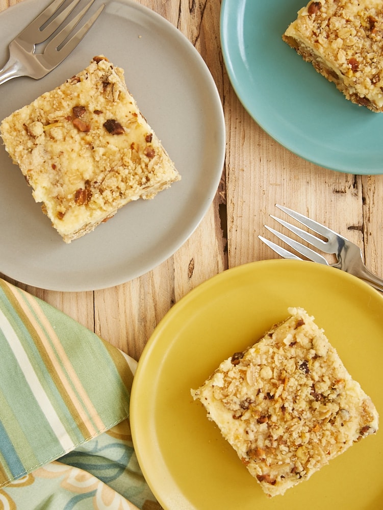 overhead view of Lemon Pistachio Cheesecake Bars on yellow, gray, and blue plates