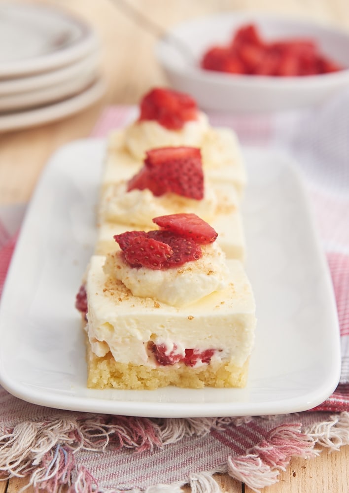 three slices of Strawberry Shortcake Cheesecake Bars lined up on a white rectangular plate